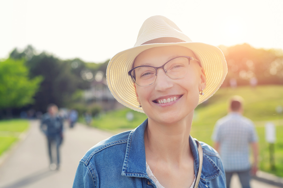 Happy young woman in hat and casual clothes enjoying life after surviving breast cancer.