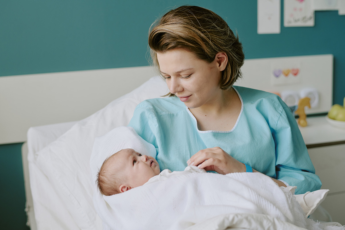 Mother holding newborn baby while smiling in hospital room.