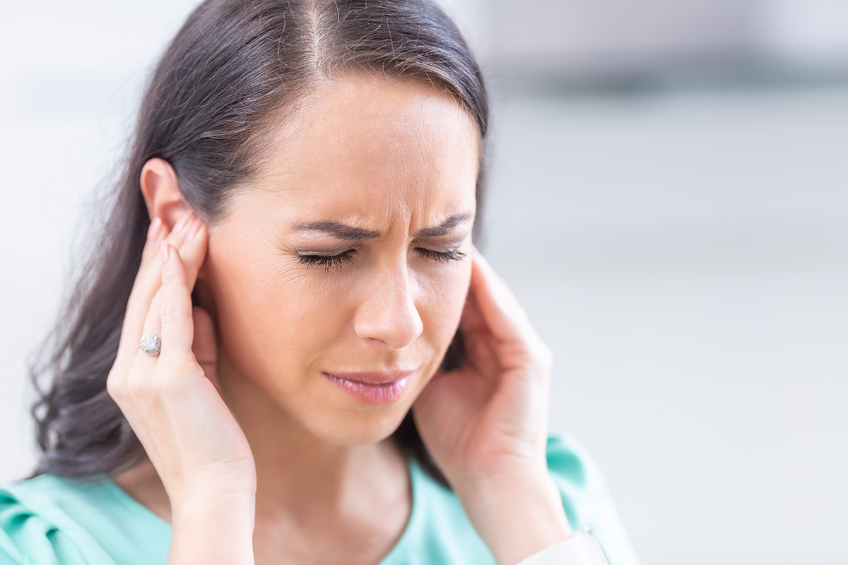Young woman suffering from tinnitus - noise ringing in her ears.